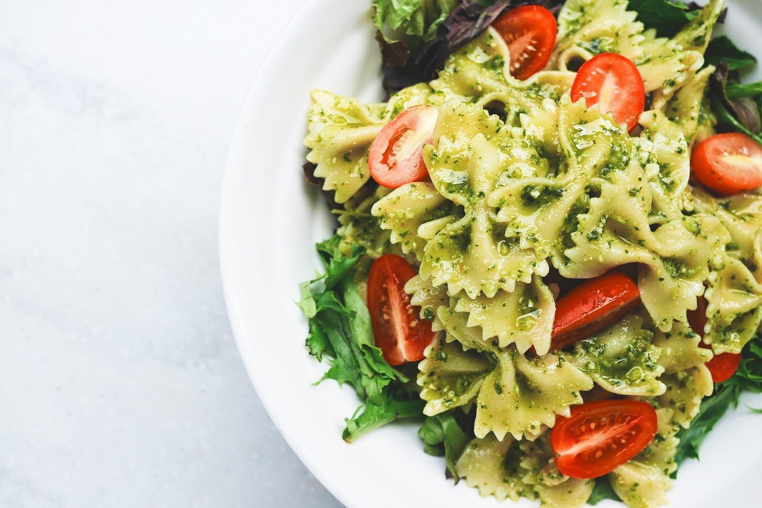 Un plato de pasta, tomates frescos y pesto verde