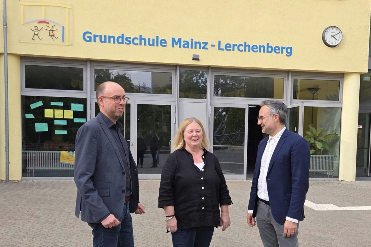 Christian Hoffmann, kierownik działu ds. klientów i relacji z opinią publiczną w Mainzer Mobilität, Susanne Millen, dyrektorka szkoły podstawowej Mainz-Lerchenberg oraz Ata Delbasteh, dyrektor ds. edukacji w stolicy kraju związkowego Moguncji, stoją przed budynkiem szkoły z napisem „Szkoła podstawowa Mainz-Lerchenberg”