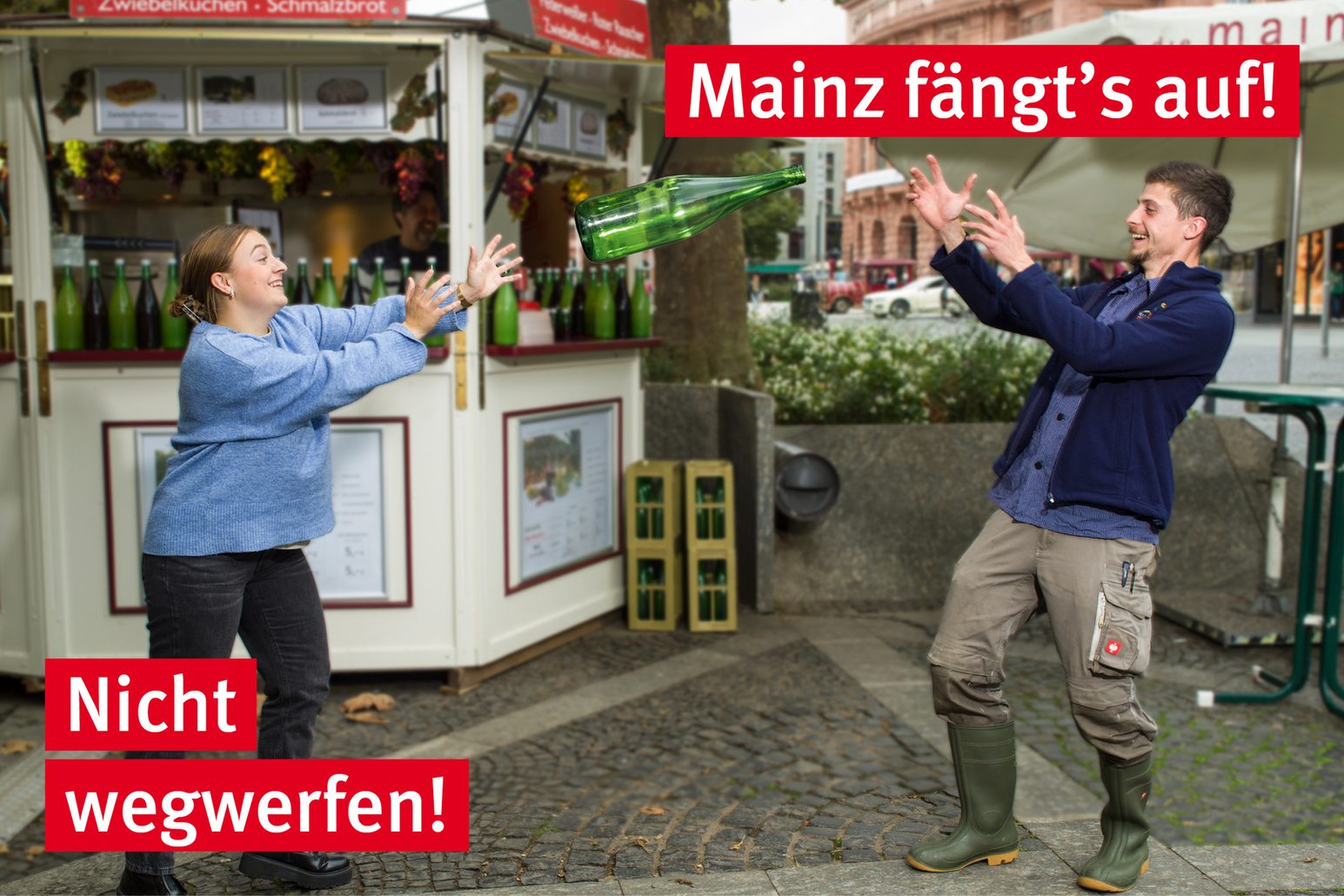 Eine Winzerin wirft einem Winzer eine Weinflasche zu.
