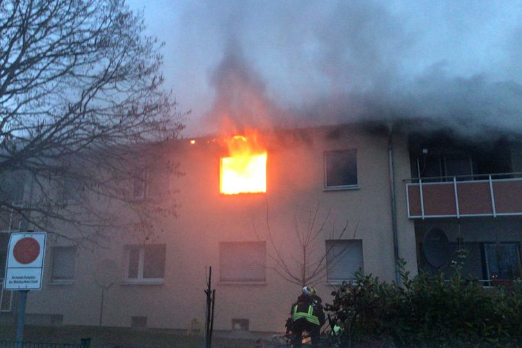 Flammen dringen aus einem Fenster im ersten Stock heraus.