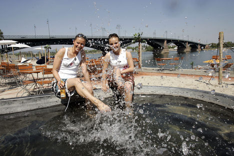Zwei Frauen sitzen am Rheinstrand und spritzen mit Wasser.