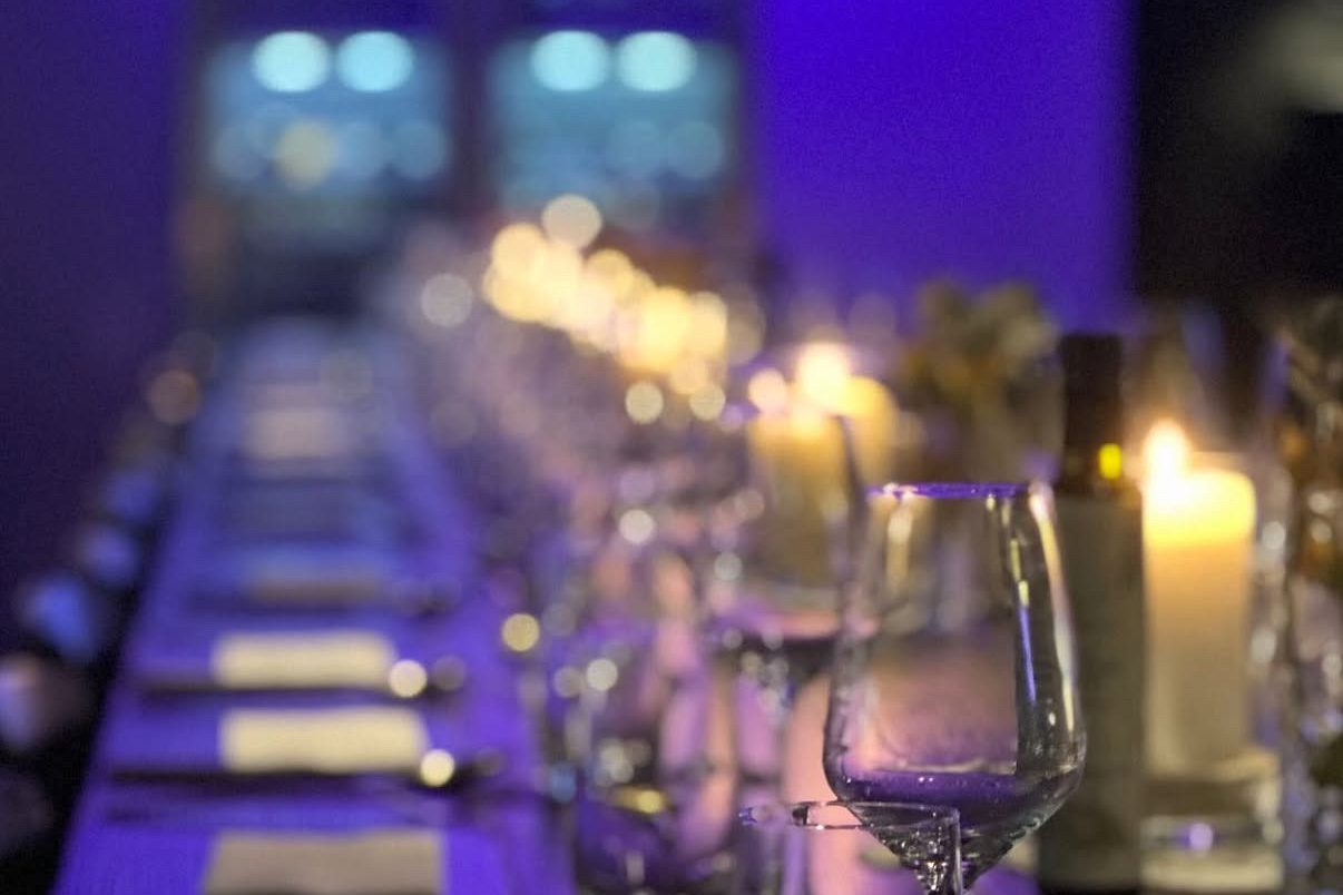 Au premier plan, on aperçoit une table dressée qui invite à s'attabler. Le mur est éclairé d'une lumière bleue et de nombreuses bougies sont allumées sur la table.