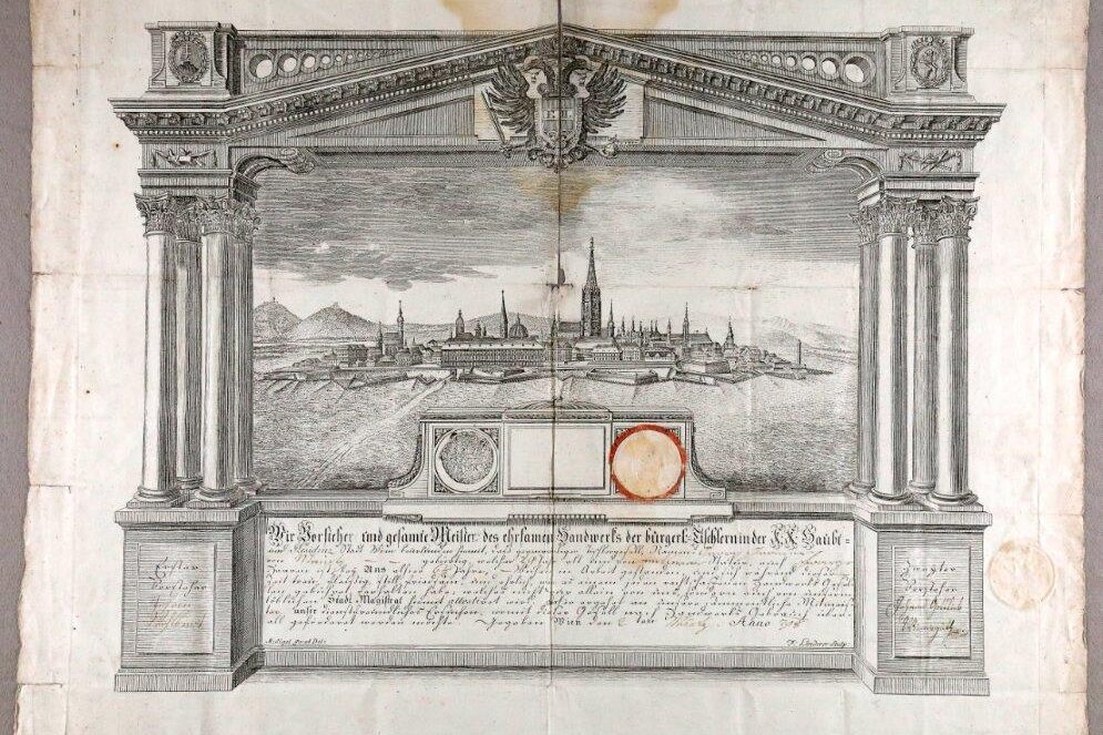Vergilbtes Papier mit Aufdruck von Stadtansicht in barockem Rahmen