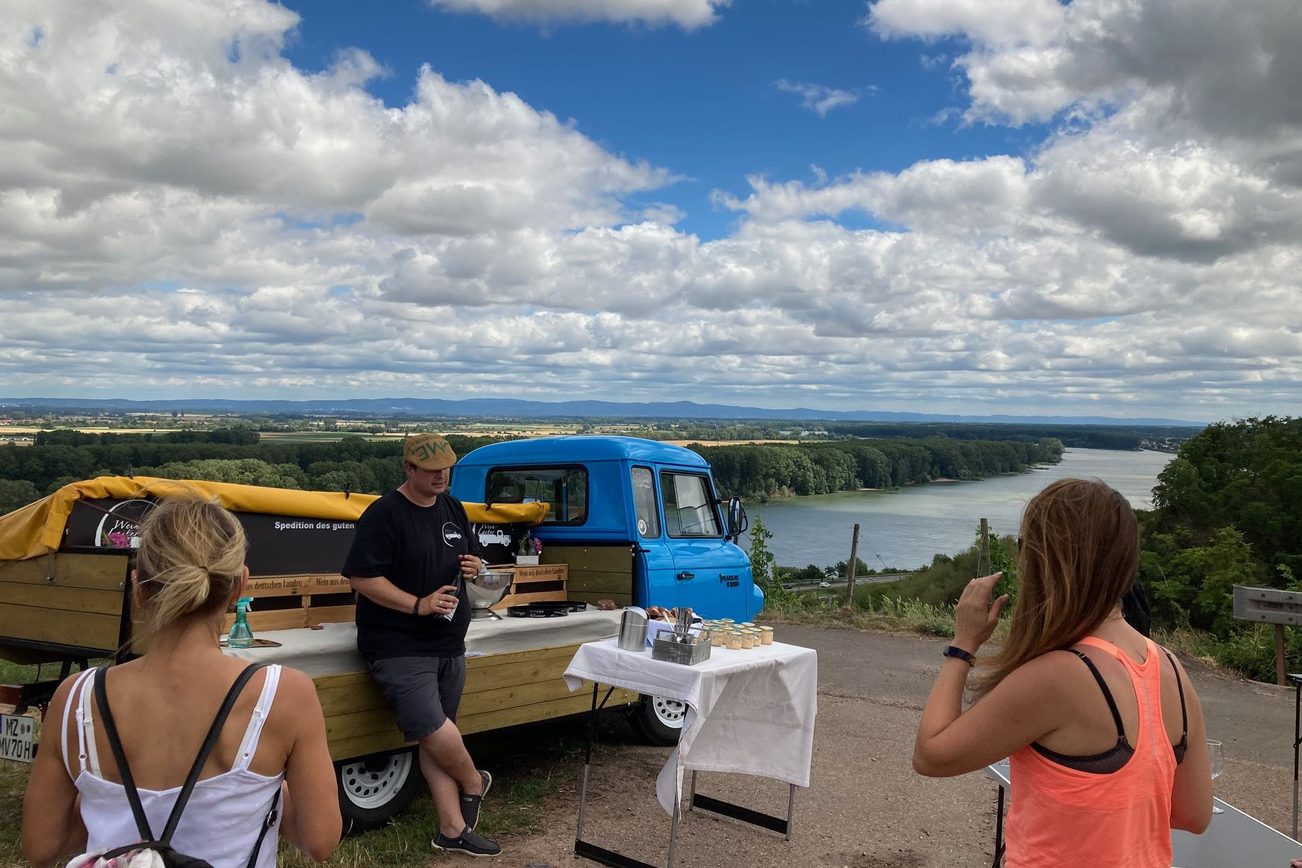 Gäste genießen Wein vom Wein-Laster mit Blick auf den Rhein