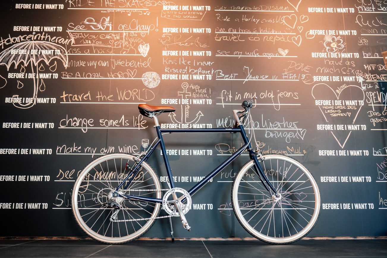 Una bicicletta si trova davanti a un muro con le frasi "Prima di morire".