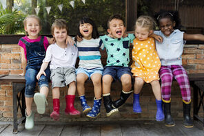 Fröhliche Kindergartenkinder auf einer Bank sitzend © AdobeStock rawpixel