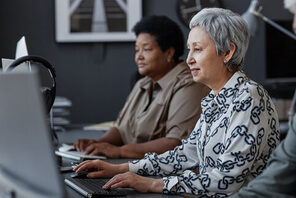 Zwei Seniorinnen sitzen an einem Schreibtisch vor Laptops © AdobeStock Seventyfour