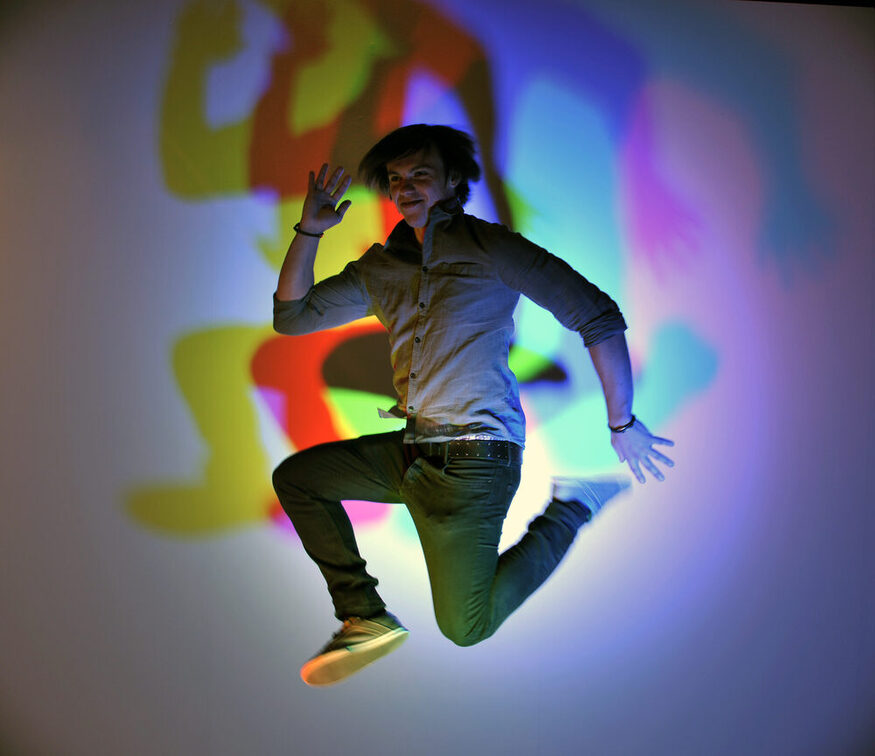 Ein Besucher springt in die Luft, hinter ihm farbige Schatten