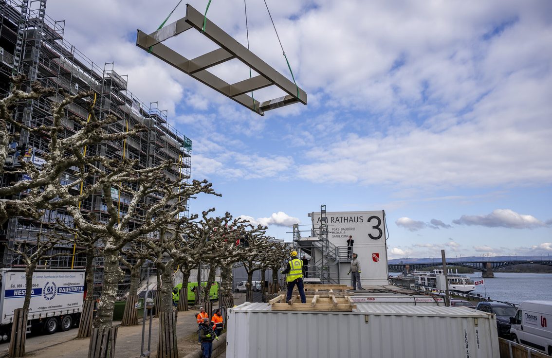 Un ouvrier du bâtiment se tient sur un conteneur au bord du Rhin Au-dessus de lui, un élément de construction est suspendu à une grue