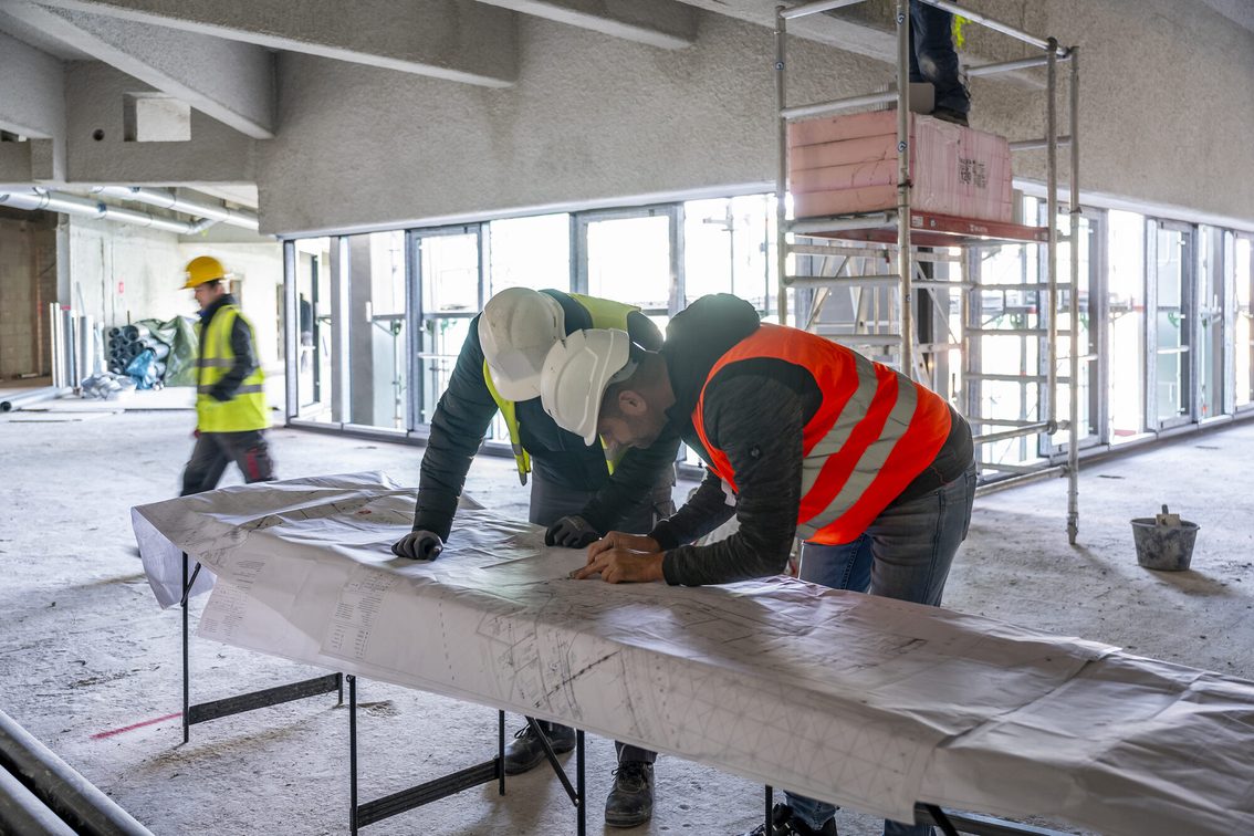 Arbeiter innen auf der Baustelle, sie schauen sich den Plan an.