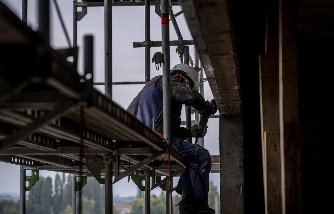 Bauarbeiter sitzt auf einem Gerüst und arbeitet an der Fassade.