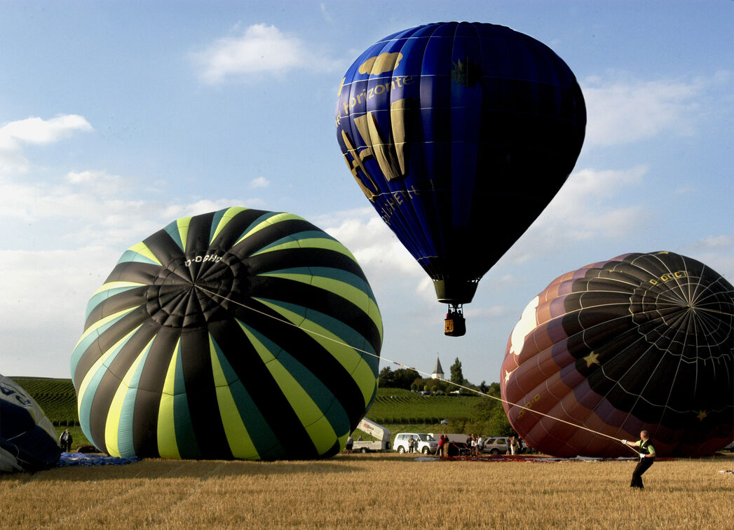 Zwei Heißluftballons liegen auf dem Boden, ein dritter hebt bereits ab.