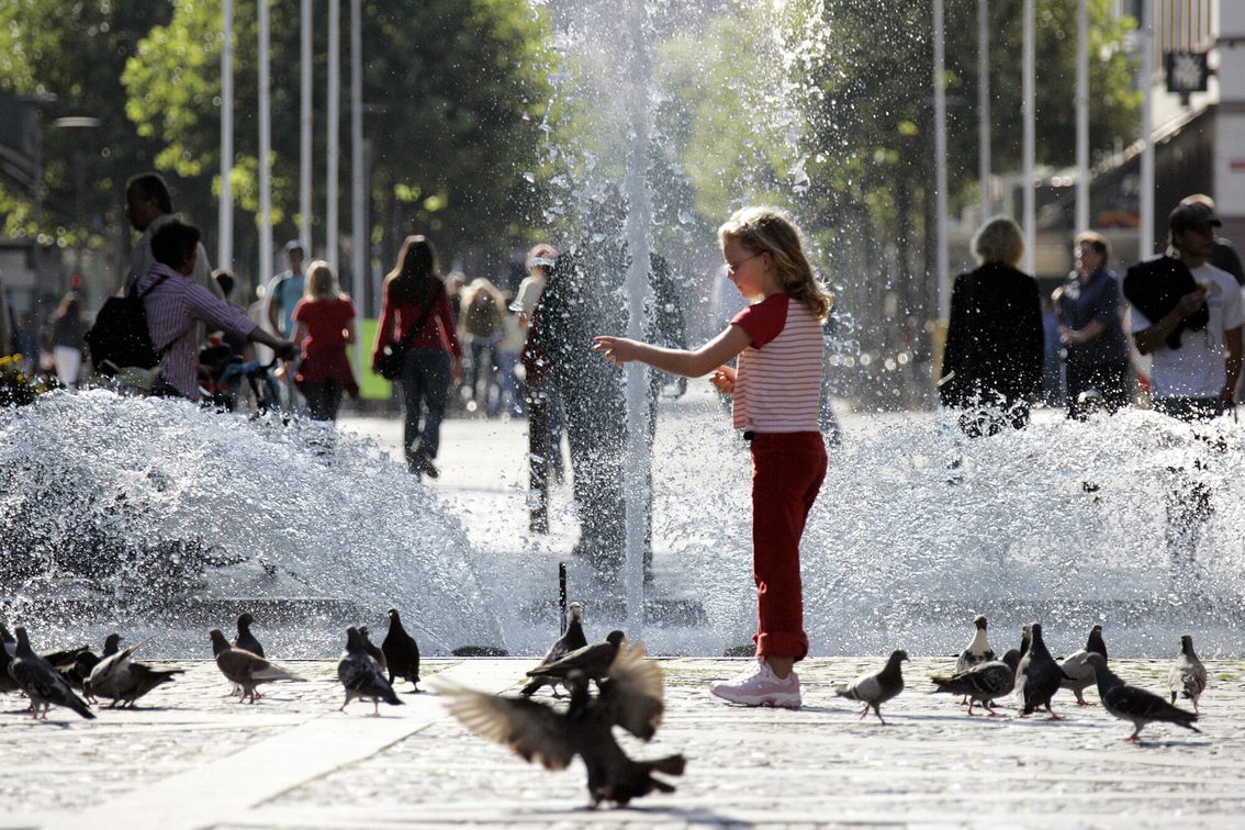 Dziewczyna karmi gołębie przed fontanną Höfchenbrunnen