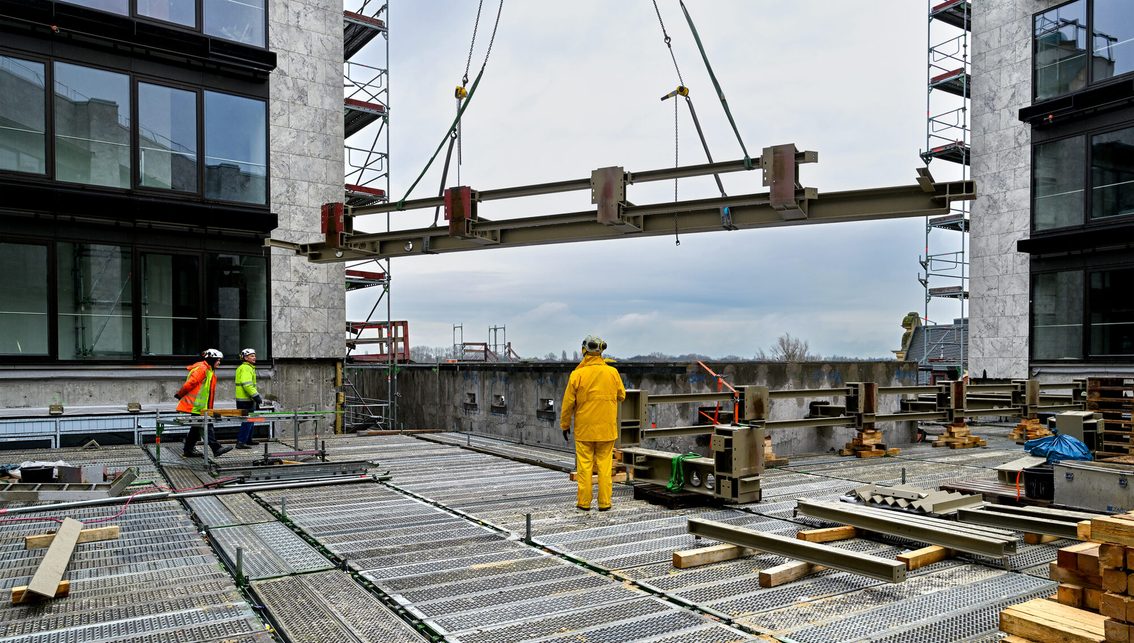 Trois ouvriers sur le chantier de l'hôtel de ville reçoivent une pièce d'acier.