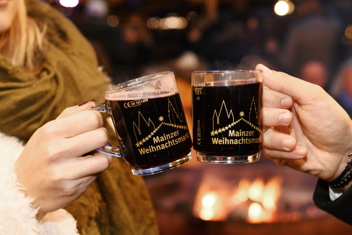 Nahaufnahme zweier Glühweintassen. Ein Paar stößt an.