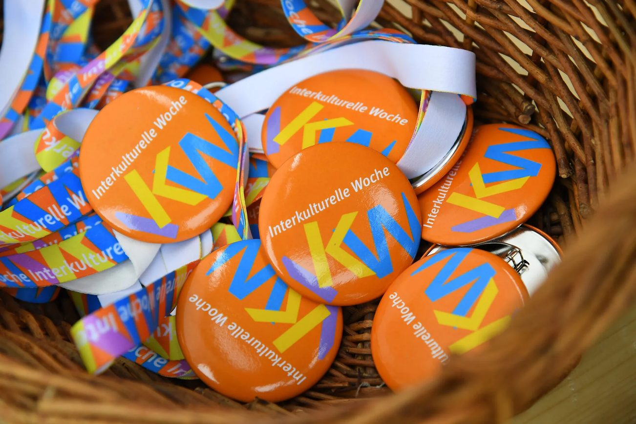Geflochtener Weidenkorb gefüllt mit organgefarbenen Buttons der "Interkulturellen Woche" (IKW)