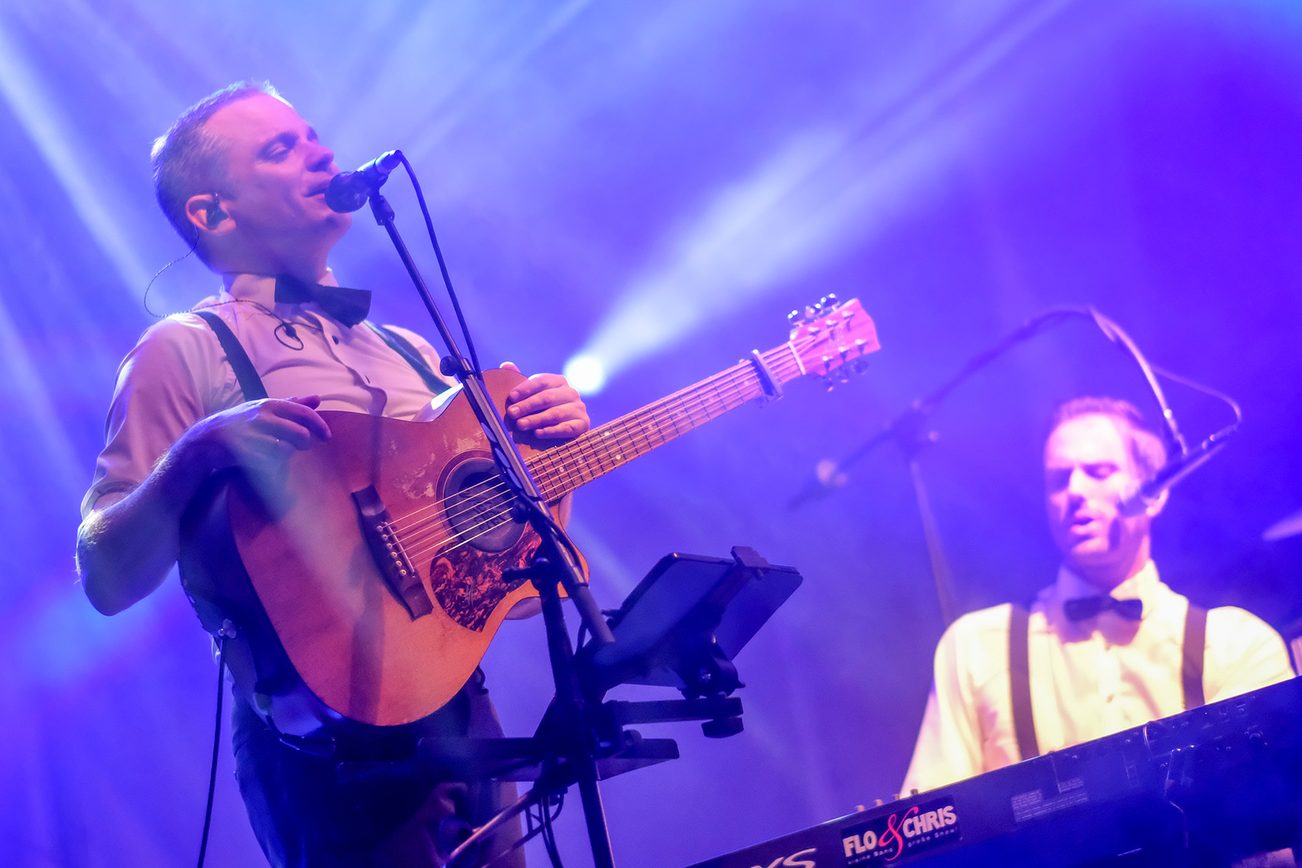 Due uomini su un palco, uno con chitarra e microfono, l'altro seduto alla tastiera.
