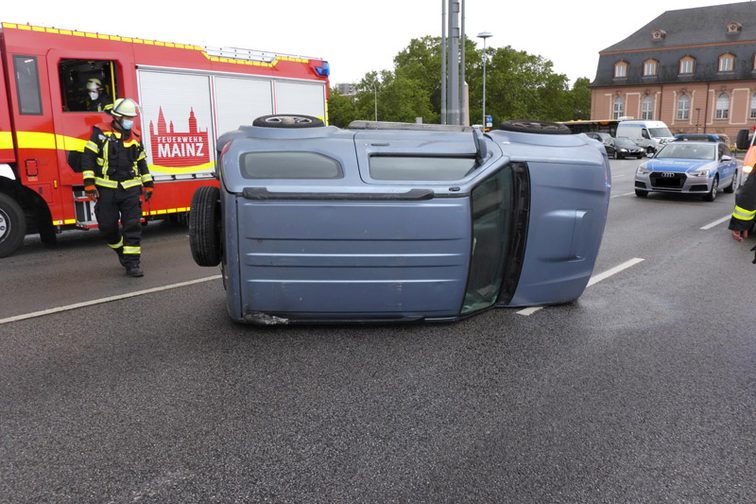 Auf der Seite liegendes Unfallfahrzeug mit Einsatzkräften im Hintergrund.