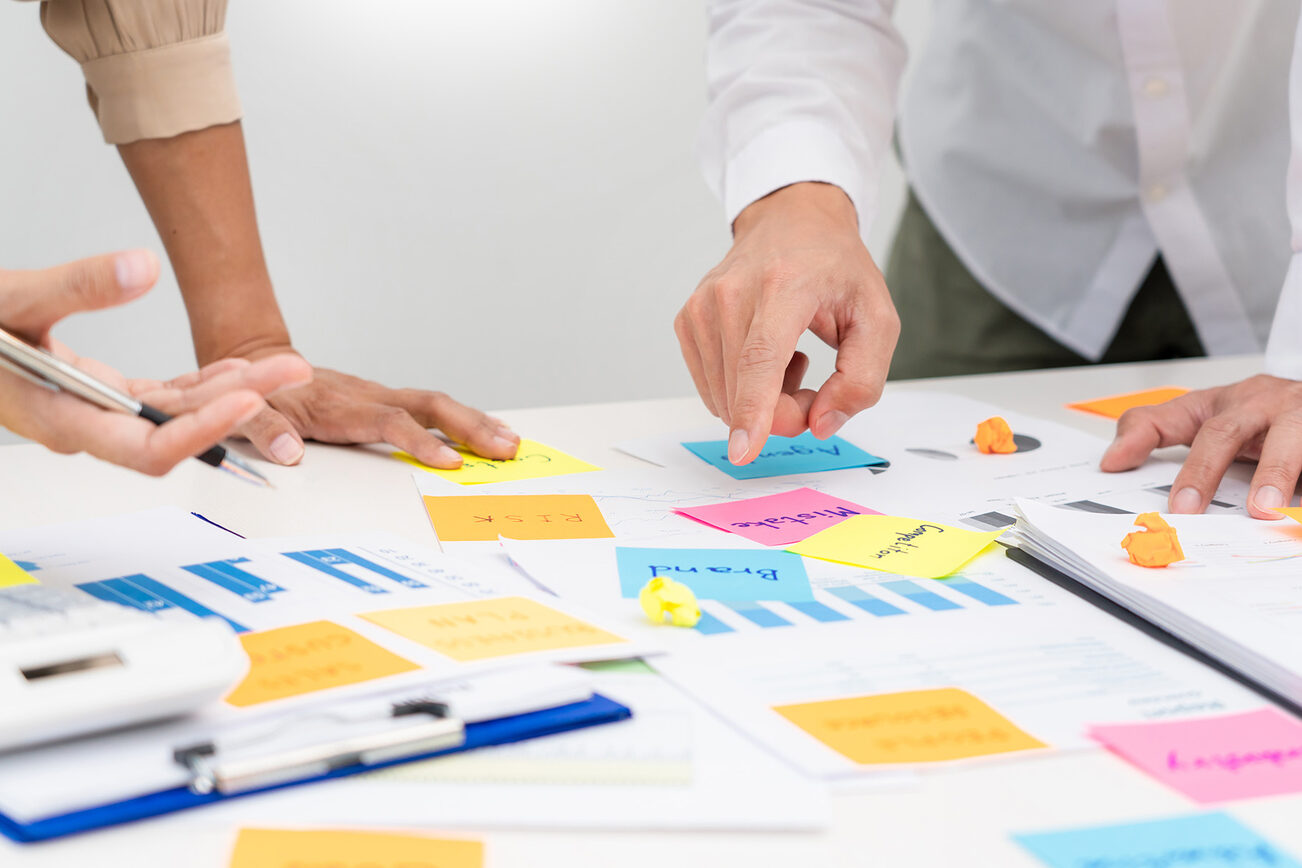 Ein Tisch mit bunten Zetteln und Menschen die sich dazu besprechen.