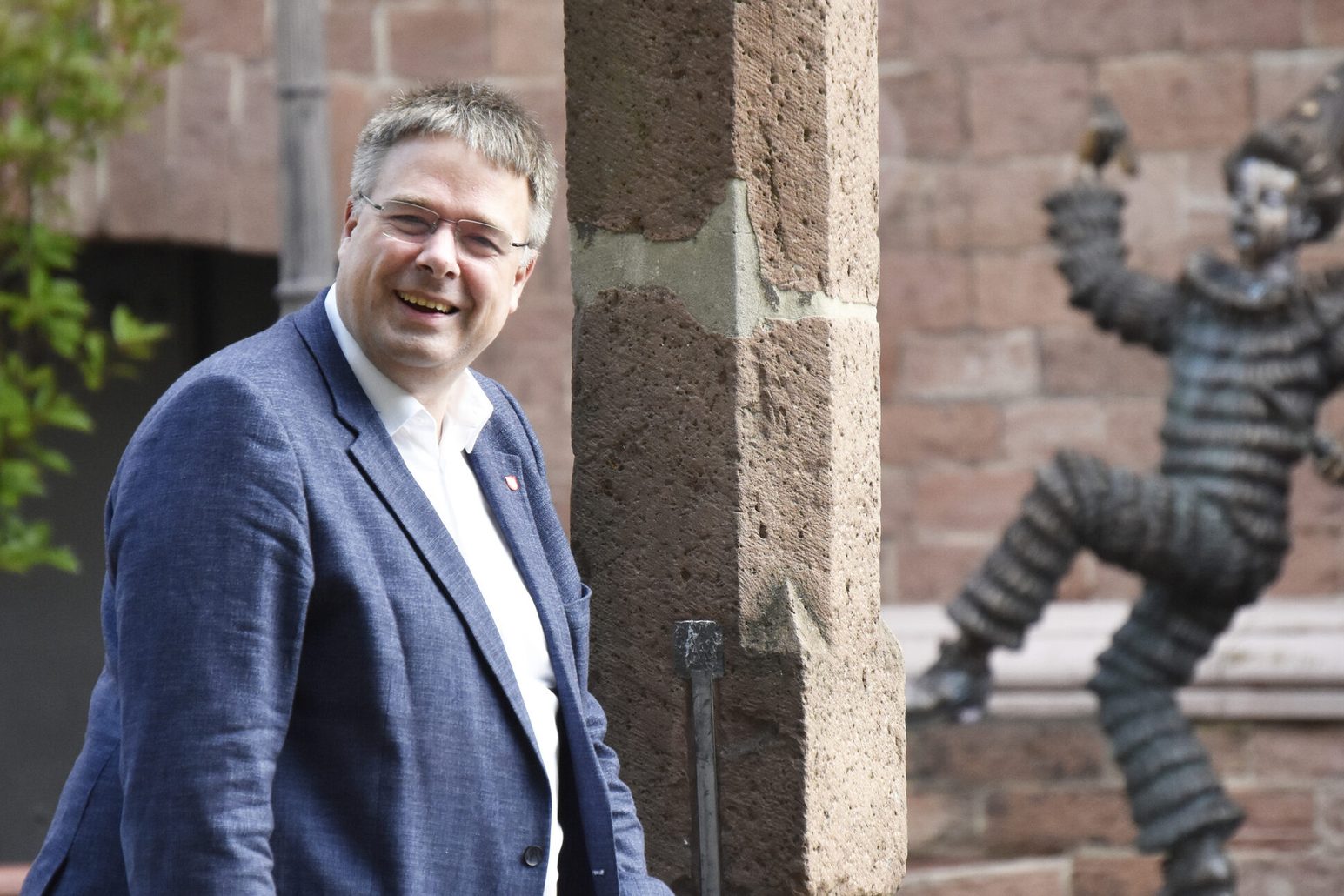 Karsten Lange sorride alla telecamera; sullo sfondo si vede la figura di un clown che balla davanti al Museo del Carnevale. Il Museo del Carnevale è il suo posto preferito a Magonza.