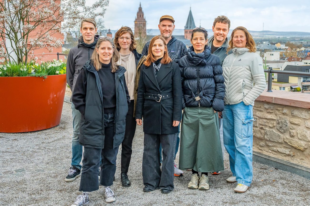 8 Personen stehen draußen, im Hintergrund Blumen und der Dom.
