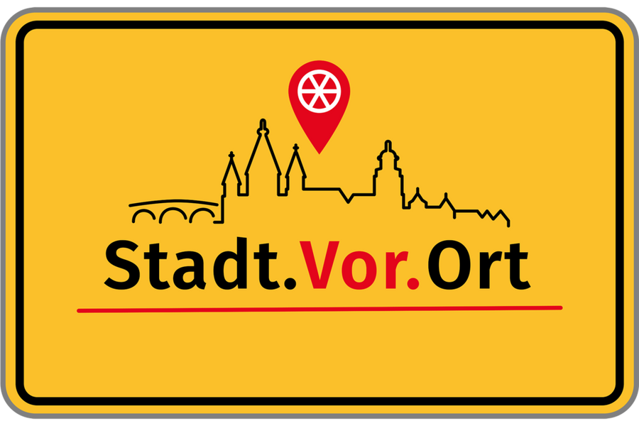 Eine Art gelbes Ortseingangsschild mit der Silhouette der Theodor-Heuss-Brücke und des Doms mit einer Ortsmarke mit einem sechsspeichigem Rad, darunter der Schriftzug: Stadt.Vor.Ort